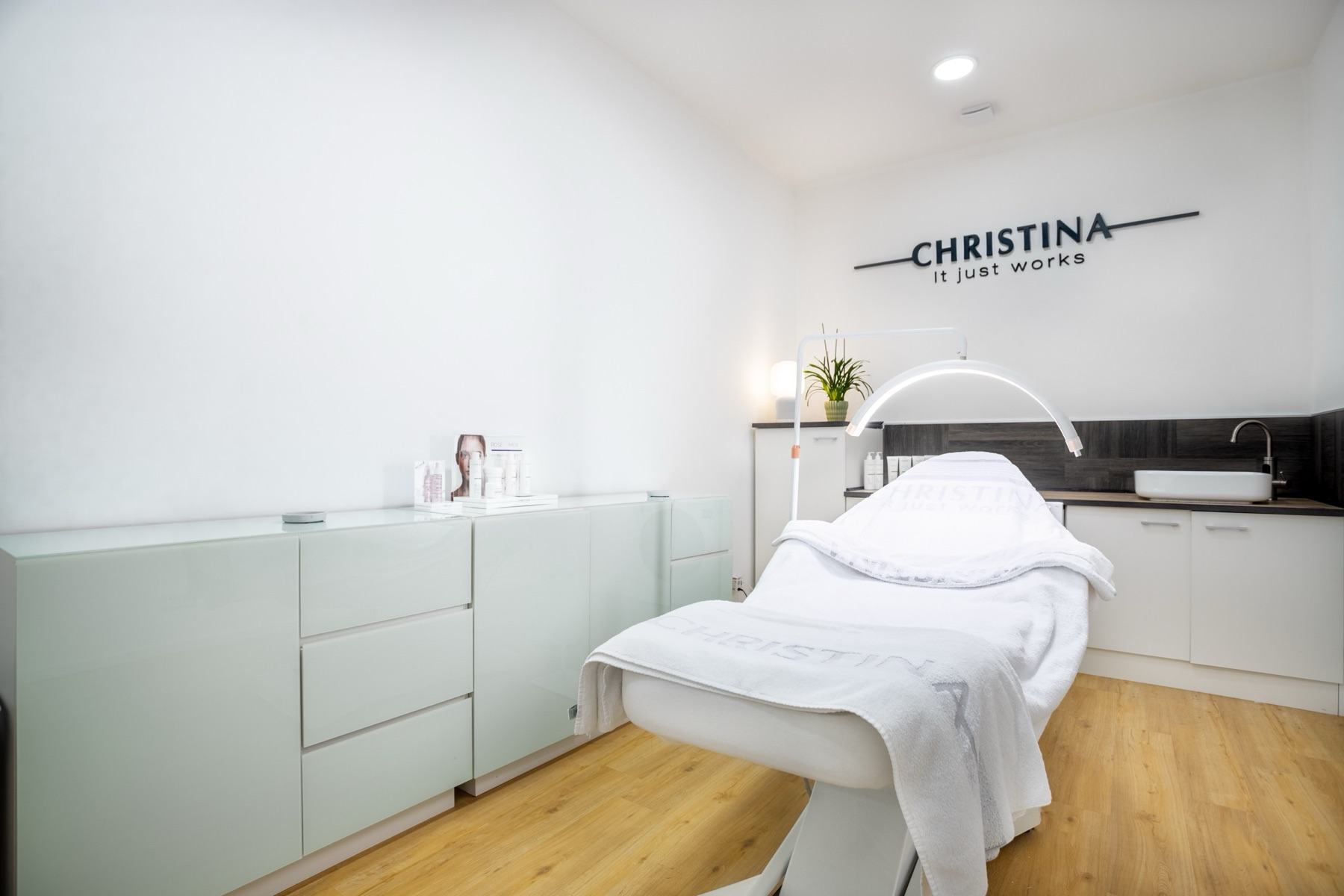 Behandlungsraum im Christina House: Behandlungsliege mit Lupenleuchte unter dem Christina-Wandlogo